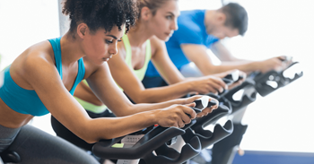 Three people are working out on exercise bikes in a gym.